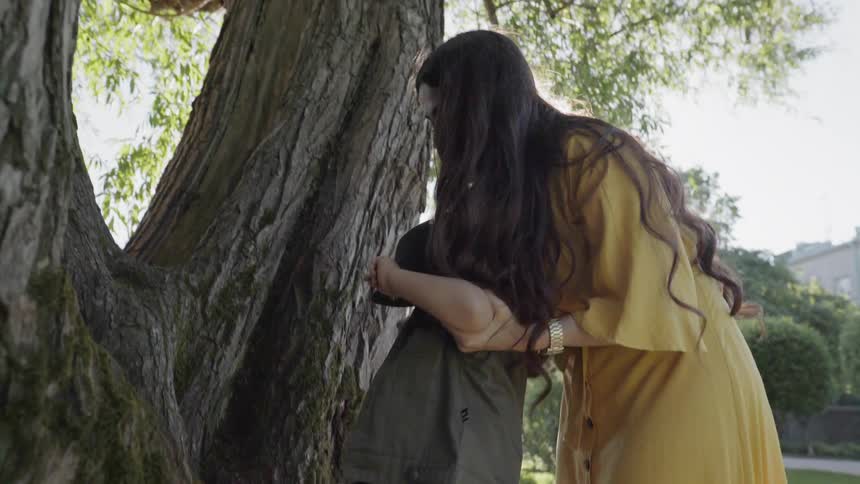A caring mother assisting her young child in climbing a large park tree.