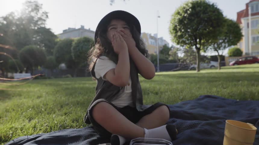 A happy child playing and laughing while sitting outdoors on a picnic blanket.