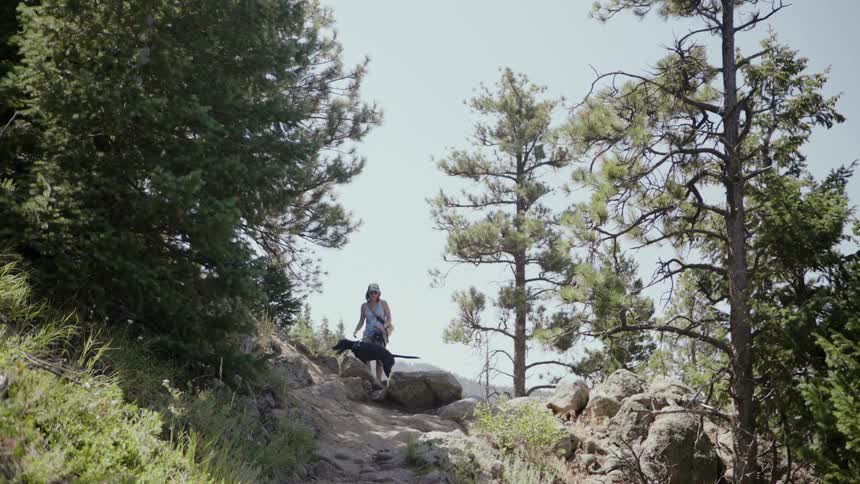 Woman walks up a rocky path on hill with her dog