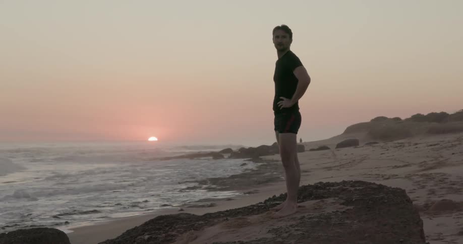 Man stands on a beach at sunset