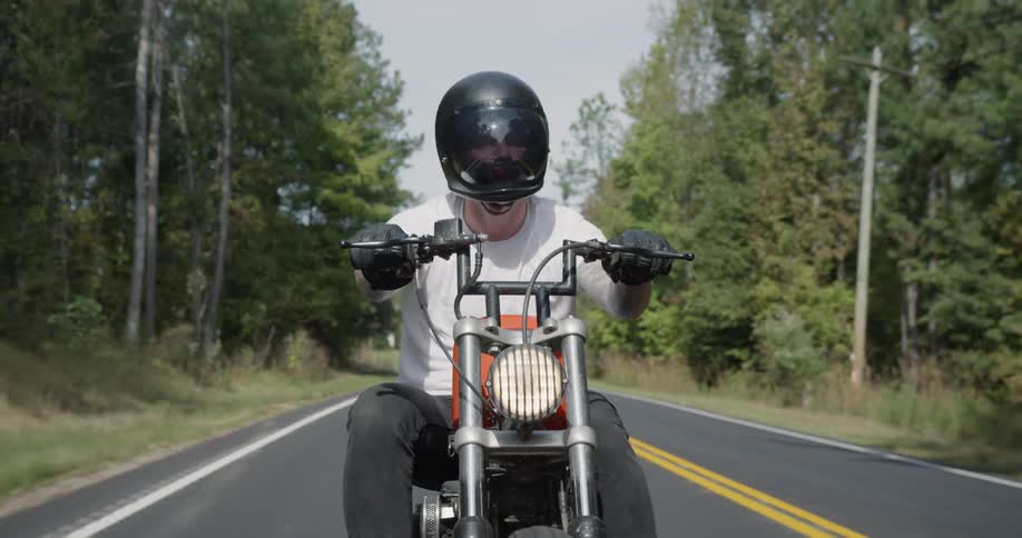 A man is riding a motorcycle on a road through a forest on a sunny day