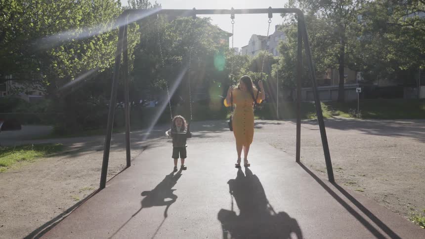 A happy mother and child swinging together on swings at park playground.