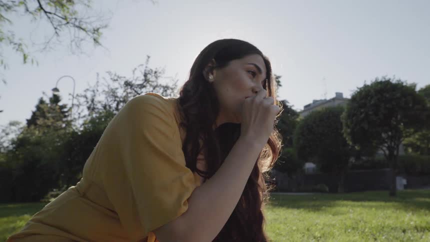 A young woman eating a fresh snack while sitting outdoors on grass.