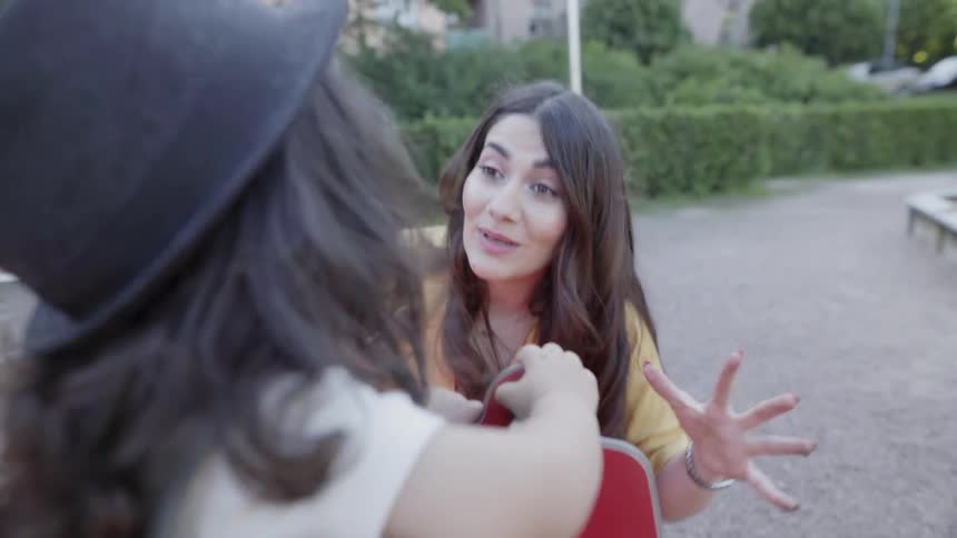 A mother gesturing playfully while talking to her child on playground rocker.