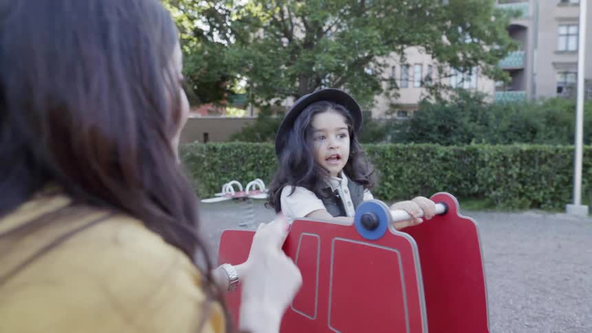 A mother is pushing her son on a playground rocker outside in daylight
