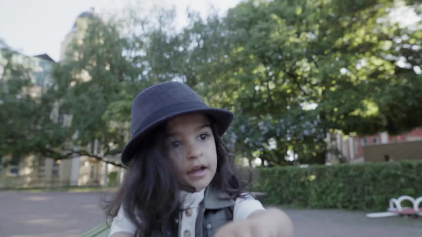 A young child wearing a black hat playing outdoors at park playground.