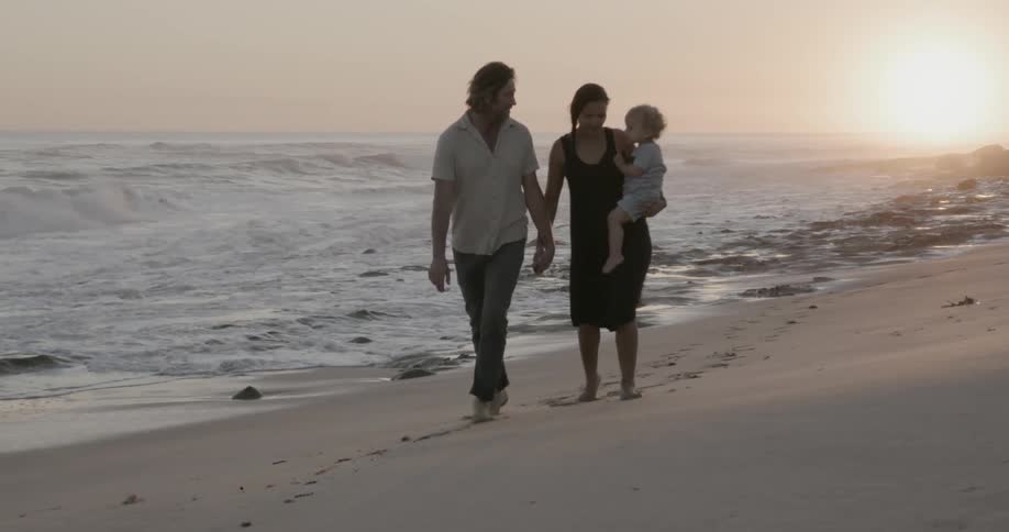 A young family walks on a beach at sunset