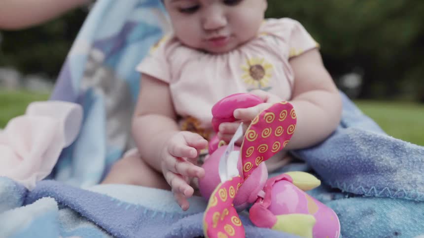 Close up of a baby playing with colorful toy on picnic blanket.