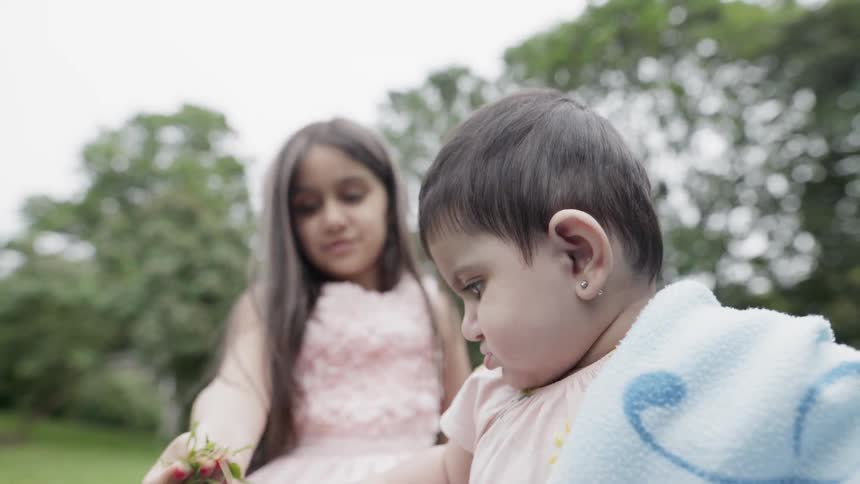 An older sister offering a piece of grass to her baby sibling outdoors.