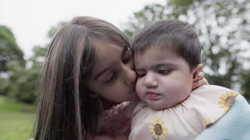 Close up of a loving sister kissing her adorable baby sibling on cheek.