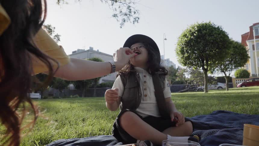 A mother feeding a small snack to her young child during park picnic.