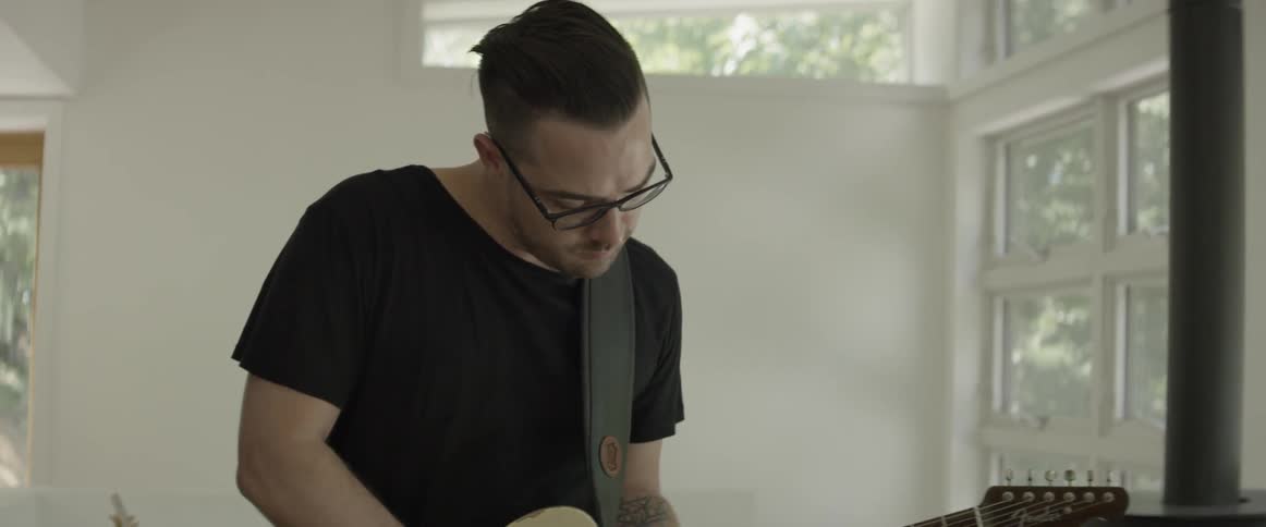 Man plays guitar in an empty room next to windows