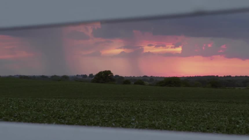 Vast flat plains with clouds pouring rain down at sunset