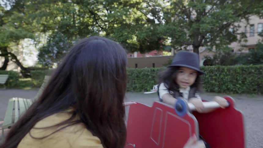 A mother watching her young child riding a spring toy at playground.