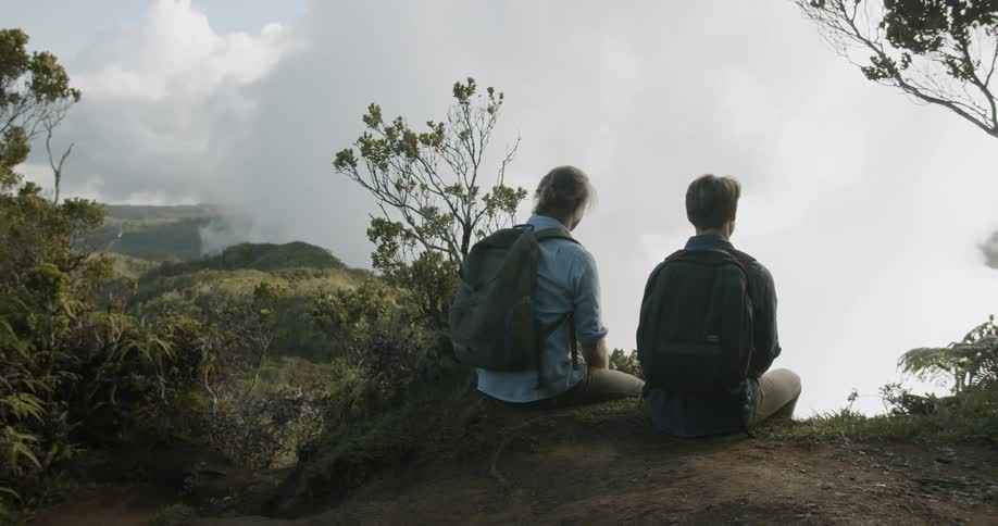 Two men sit on a ledge while hiking in mountains
