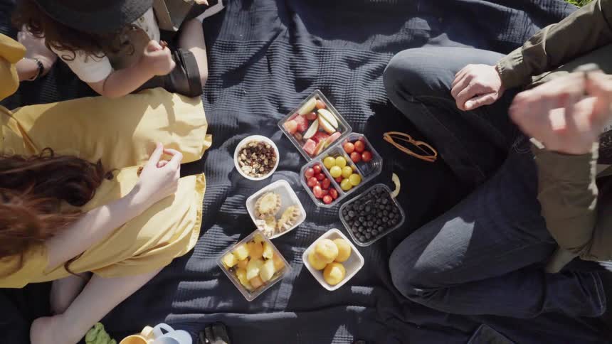 A family sharing fresh fruits and snacks spread out on picnic blanket.