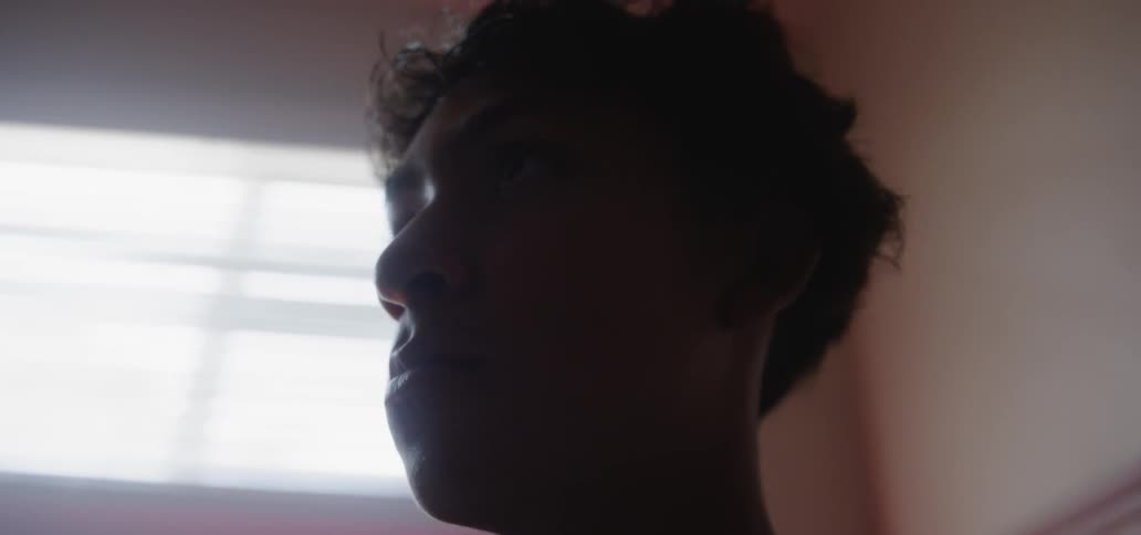 A man stands near the window in a dark room