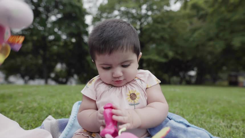 Cute baby sitting on blanket holding a colorful toy during park picnic.