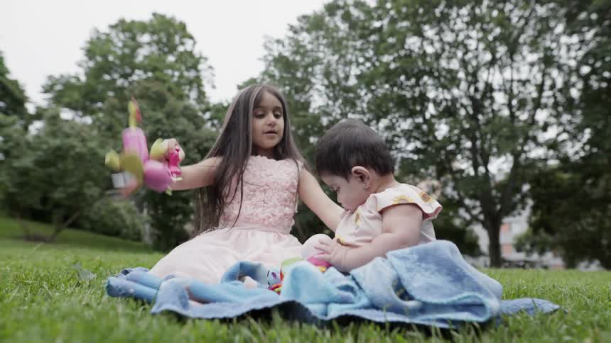 Loving older sister shaking a colorful rattle toy to entertain her baby sibling.