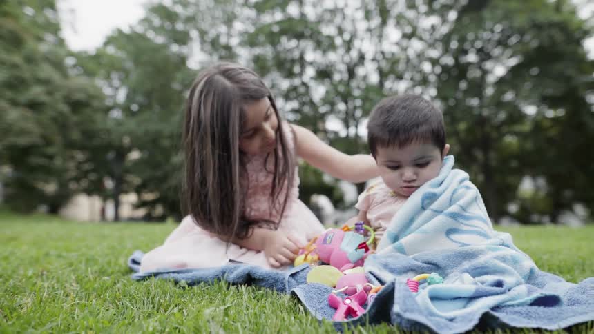 An older sister affectionately placing a hand on baby sibling during picnic.