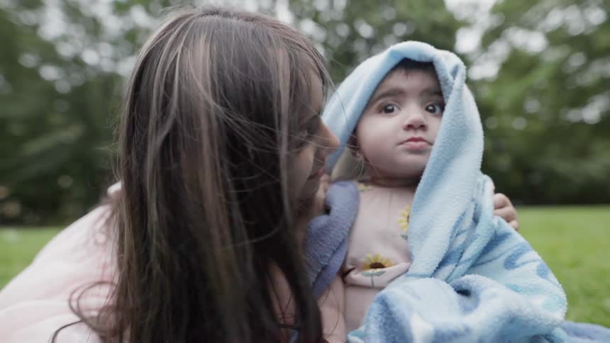 Little girl wraps her baby sibling in a blanket outside in the grass