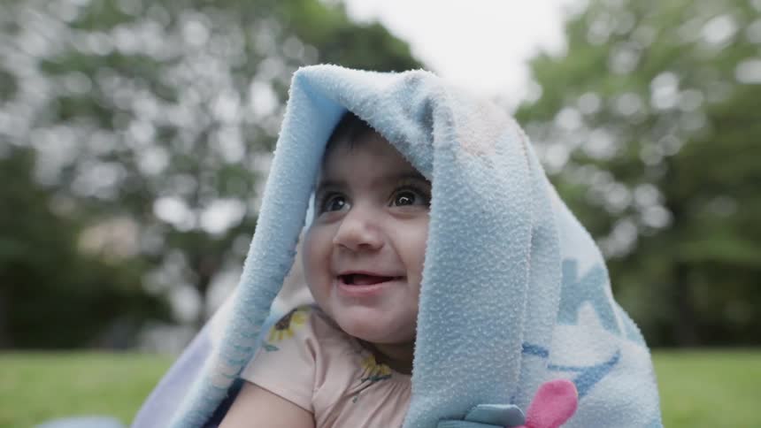 Baby covered in a blanket touches the grass