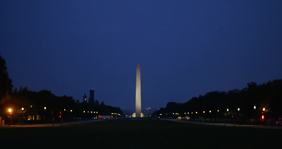 Trucks and traffic travel past the washington monument at night