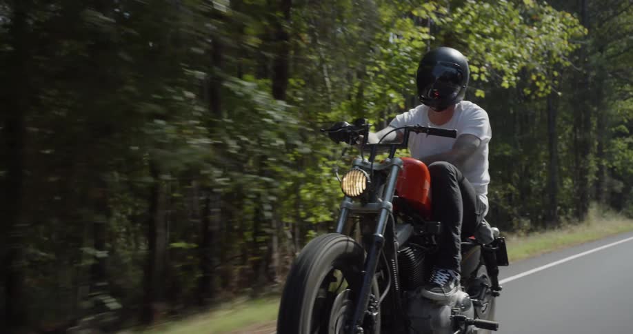 A man motorcycles on a tree-lined road