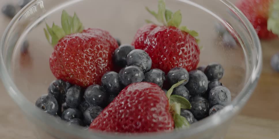 Strawberries and blueberries sit in a glass bowl