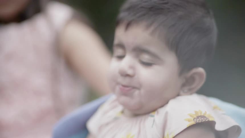 Adorable baby closing eyes with a sweet content expression during a park picnic.