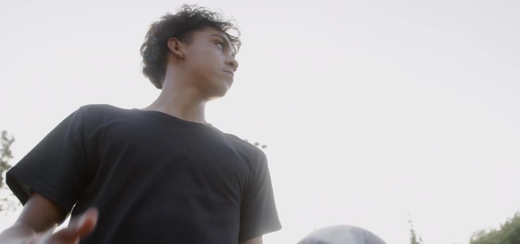 A teenager plays soccer outside on a sunny day