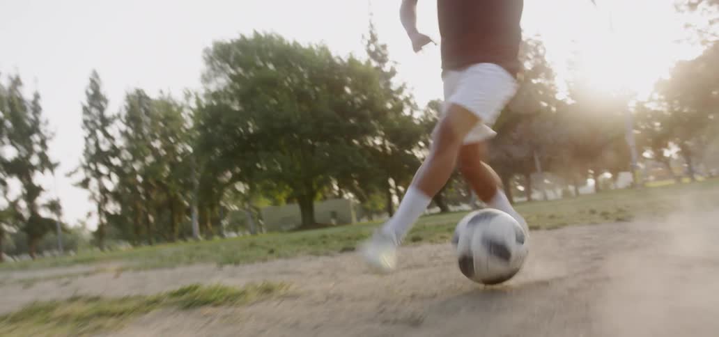 Person is kicking soccer ball in field as sun sets