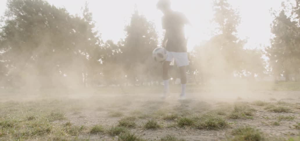 Boy kicks soccer ball in the air in dusty field