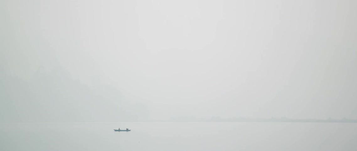 Two people are sitting in canoe on body of water on foggy day