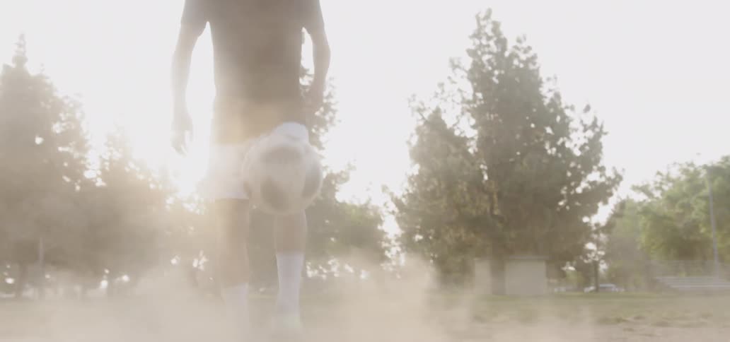 Boy is kicking soccer ball into the air on dusty field