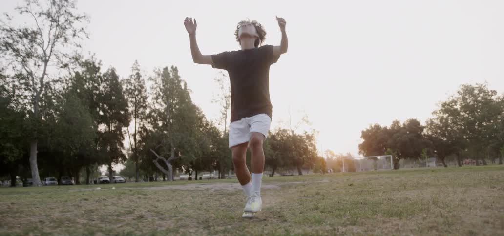 Boy is kicking and head butting soccer ball as sun sets