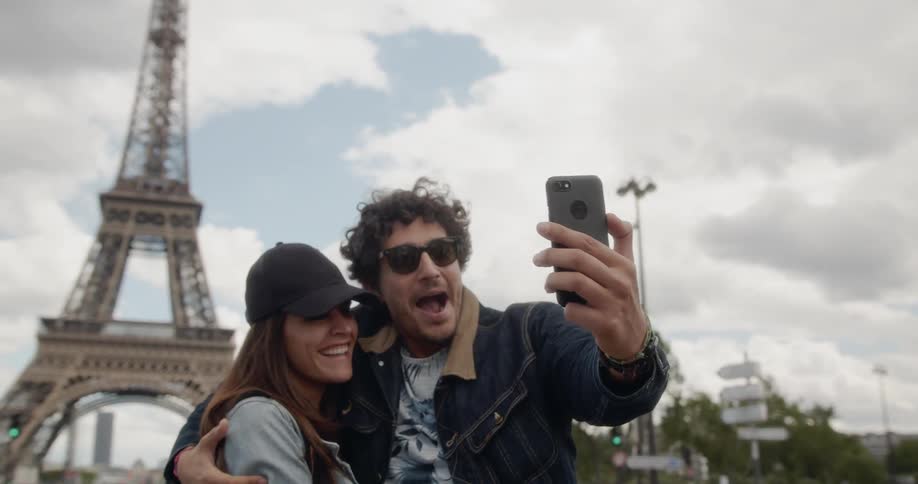 A man and woman photograph themselves in front of the eiffel tower