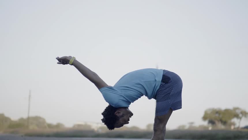 A man bends over while stretching his arms outside