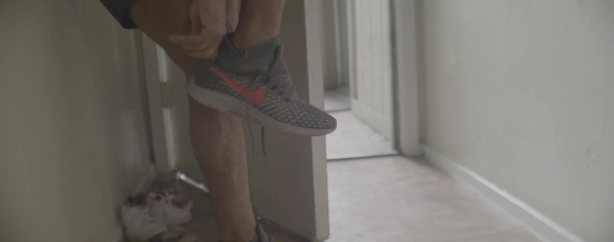 A man puts on his running shoe then bends to tie it