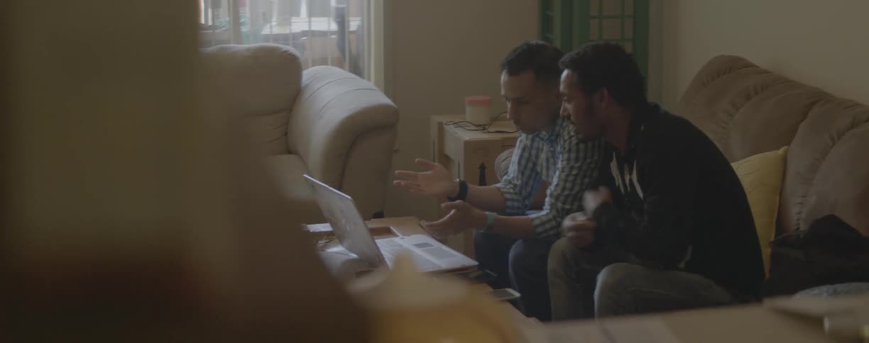 Two men use a laptop on the couch