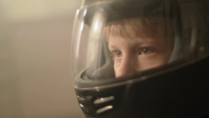 A young boy pretends to drive while wearing a helmet