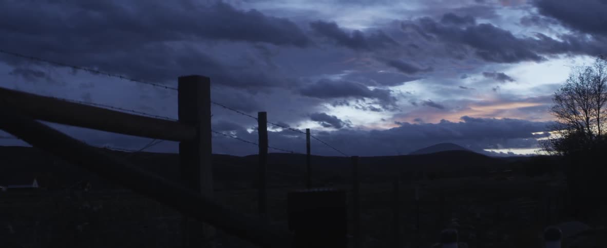 Clouds float over a silhouetted barbed wire fence