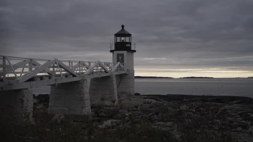View of a lighthouse, shoreline and a body of water on a cloudy day