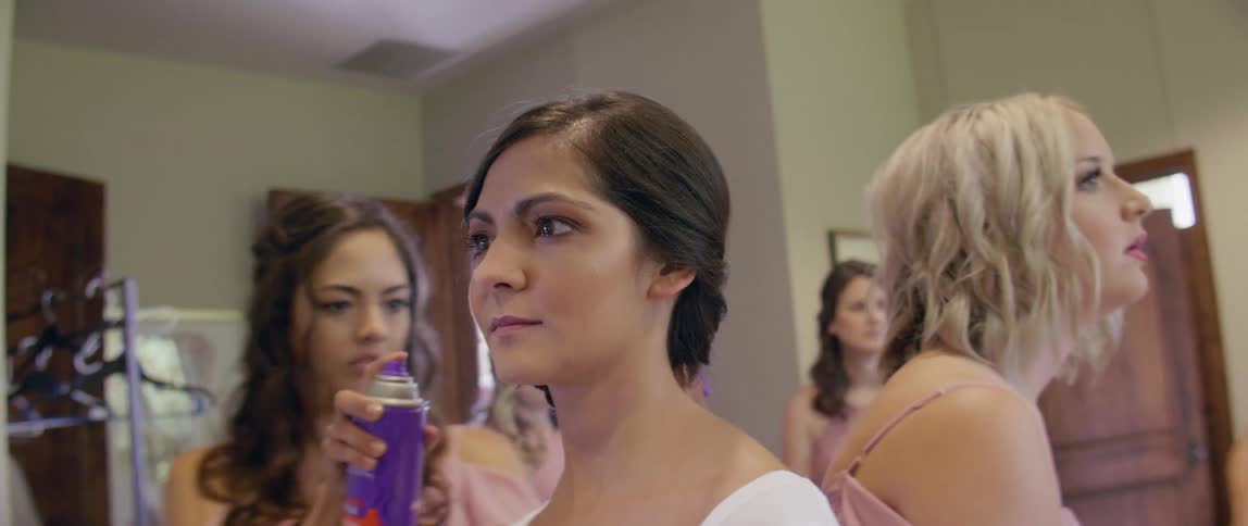 A bride has her hair styled in a dressing groom