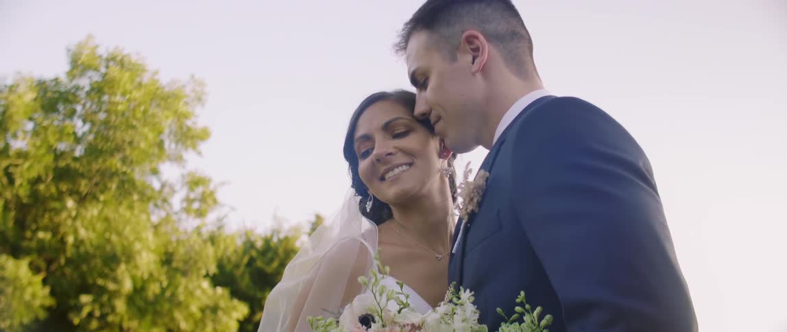 A bride and groom smile as they pose for photographs outside