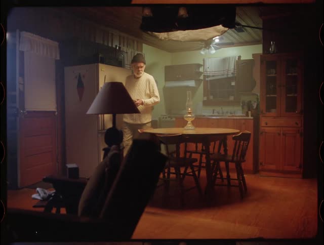 An old man is setting plates on a table inside his home at night