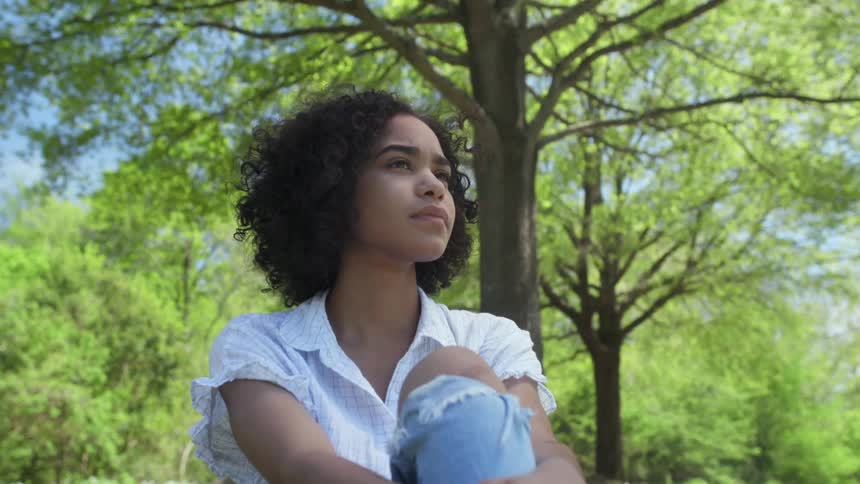 A woman sits under the trees on a sunny day