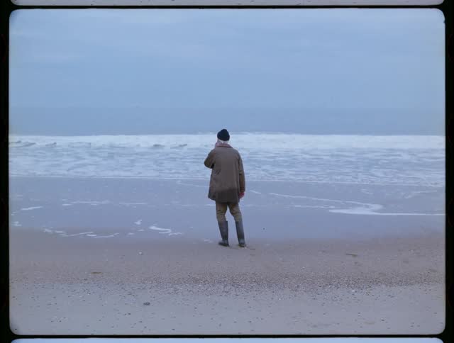 An elderly man stands alone on a beach