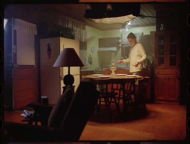 An elderly man sets a dining room table