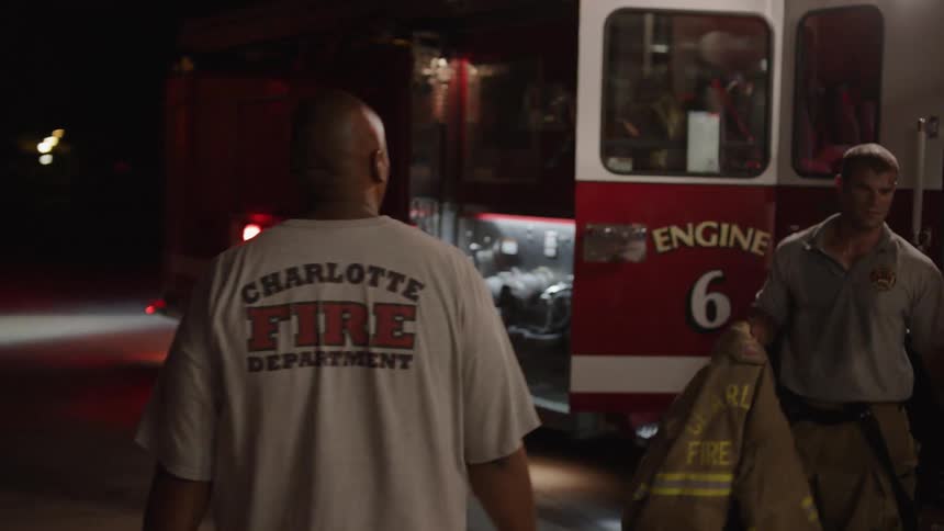 A firefighter is greeting  a firetruck as it returns to the station at night
